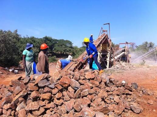 Workers sorting mined material near a processing plant